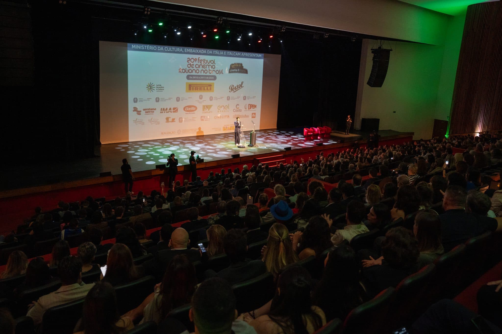 Auditório lotado durante evento da ITALCAM, com plateia e telão de patrocinadores