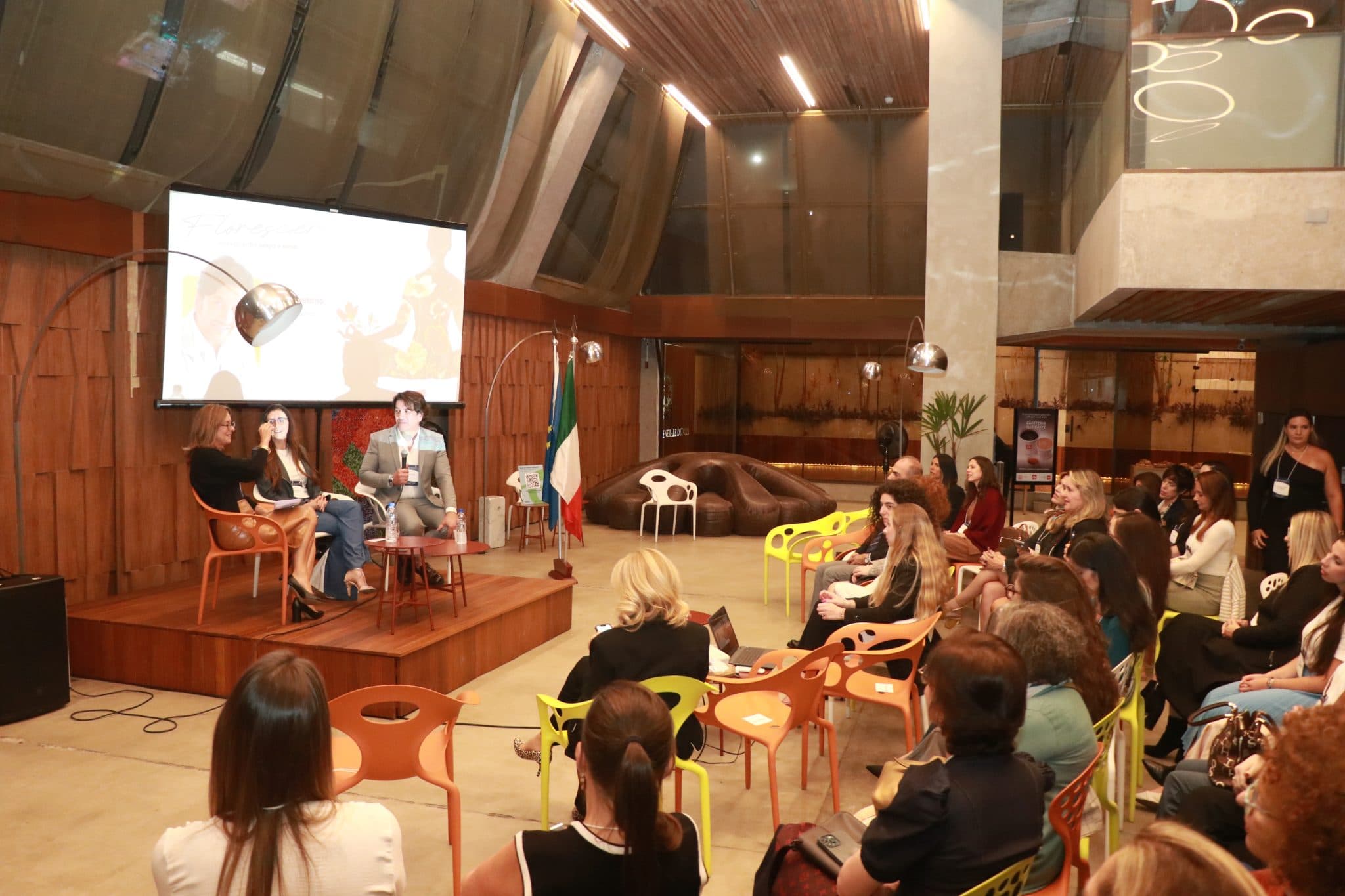 Painel de debate com especialistas no palco de um evento da ITALCAM, com a bandeira da Itália ao fundo